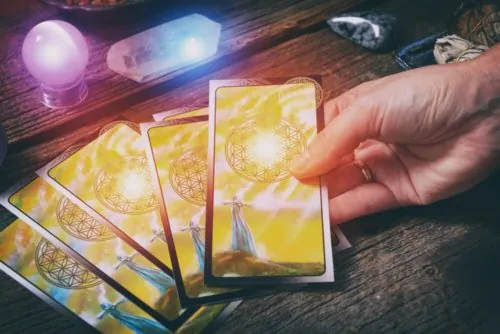 Mano sosteniendo cartas de tarot doradas junto a cuarzos sobre una mesa de madera